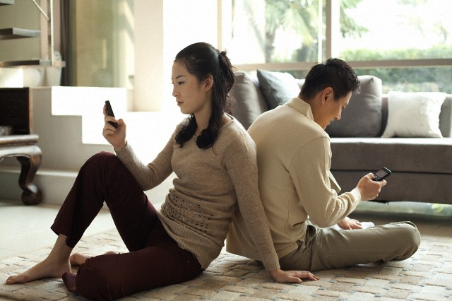 A young couple sitting back-to-back, checking their text messages.